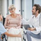 Successful doctor and young nurse talking with their senior female wheelchair-bound patient.